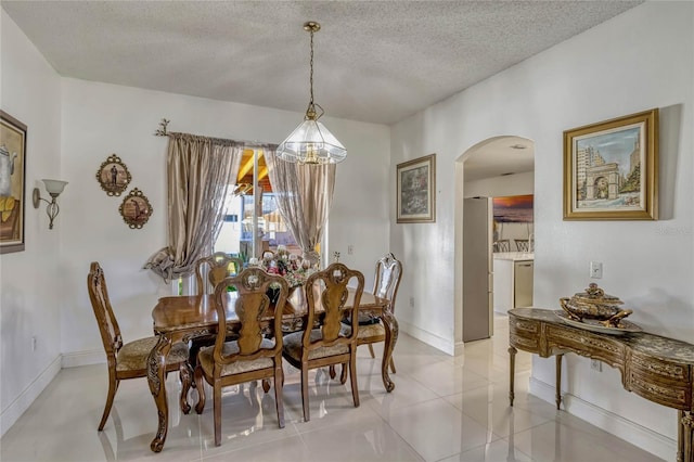 dining area with light tile patterned floors, baseboards, arched walkways, and a textured ceiling