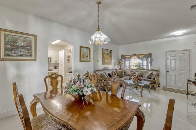 dining area featuring light tile patterned floors, visible vents, arched walkways, and a textured ceiling