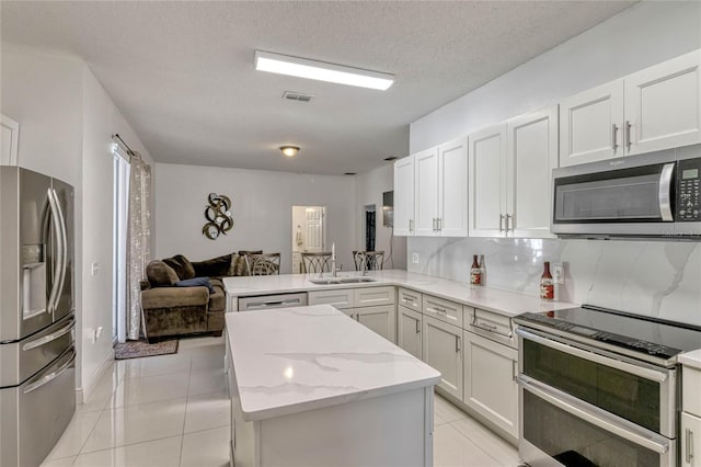 kitchen featuring light tile patterned flooring, stainless steel appliances, a peninsula, a sink, and open floor plan