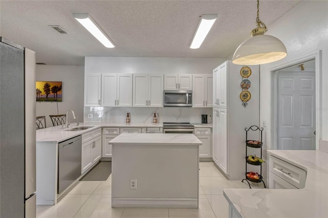 kitchen featuring appliances with stainless steel finishes, light stone countertops, white cabinetry, pendant lighting, and a sink