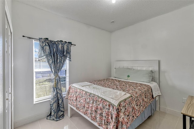 bedroom with light tile patterned floors, a textured ceiling, and baseboards