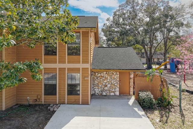 exterior space with stone siding, roof with shingles, and fence