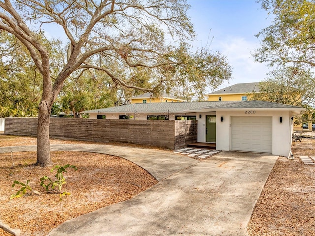 mid-century inspired home with a garage, a shingled roof, fence, driveway, and stucco siding