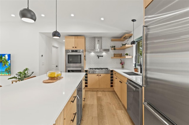 kitchen with light countertops, hanging light fixtures, appliances with stainless steel finishes, light brown cabinets, and wall chimney range hood