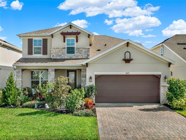 traditional home featuring an attached garage, stone siding, decorative driveway, stucco siding, and a front yard