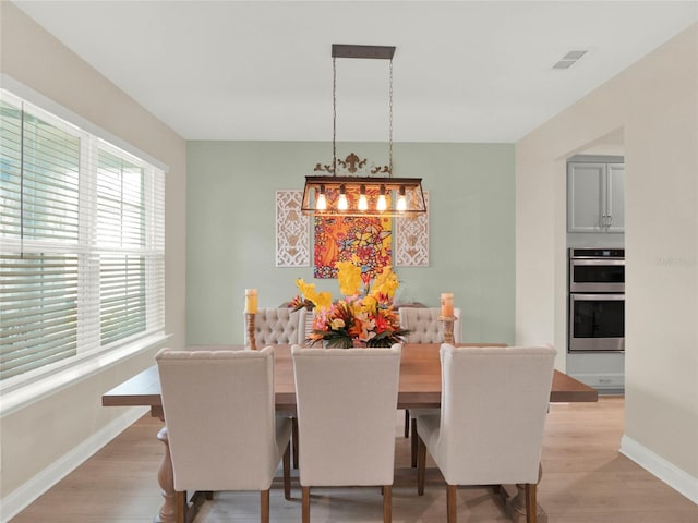 dining space with baseboards, visible vents, and light wood finished floors