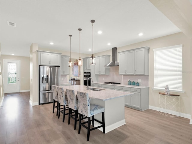 kitchen featuring visible vents, appliances with stainless steel finishes, a kitchen island with sink, wall chimney range hood, and a sink