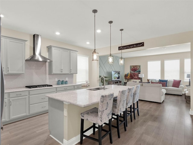 kitchen with a breakfast bar, open floor plan, wall chimney range hood, stainless steel gas stovetop, and a sink