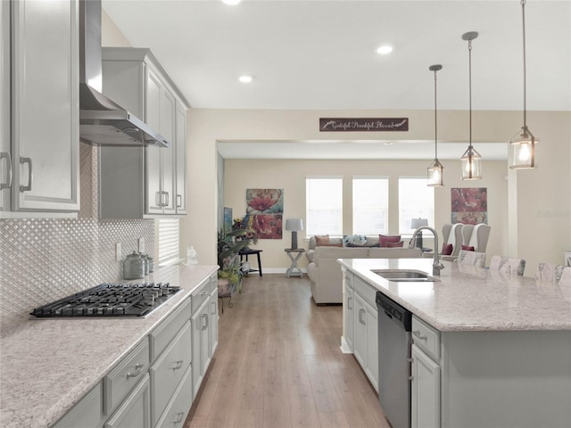 kitchen featuring pendant lighting, appliances with stainless steel finishes, open floor plan, a sink, and wall chimney range hood