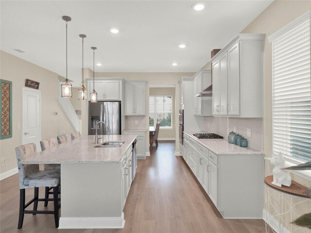 kitchen with a center island with sink, hanging light fixtures, appliances with stainless steel finishes, white cabinetry, and a sink