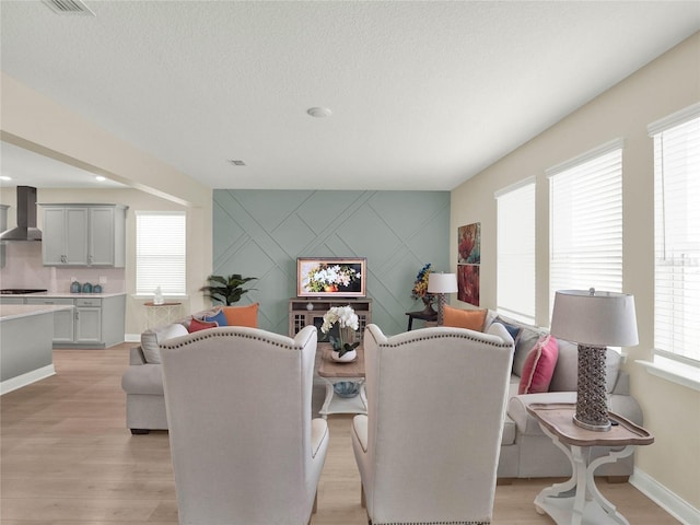 dining area featuring an accent wall, light wood-style flooring, baseboards, and a textured ceiling