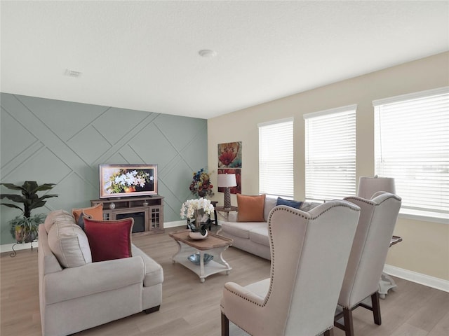 living room featuring an accent wall, baseboards, and light wood finished floors