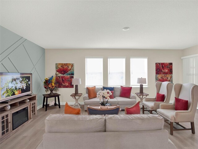 living room with a glass covered fireplace, baseboards, and light wood finished floors