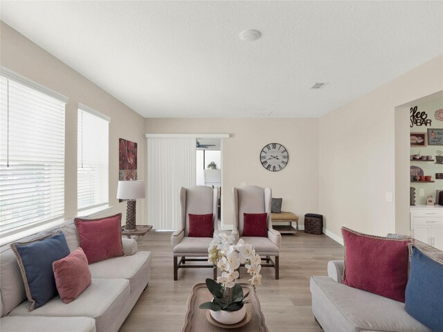 living room with light wood finished floors, baseboards, visible vents, and a textured ceiling