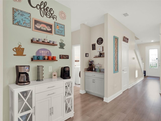 bar featuring washer / dryer, light wood-type flooring, visible vents, and baseboards