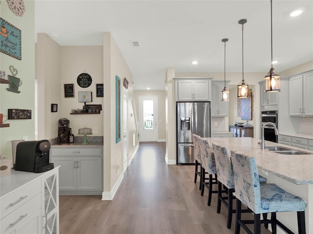 kitchen with a sink, light wood-style floors, a kitchen breakfast bar, hanging light fixtures, and appliances with stainless steel finishes