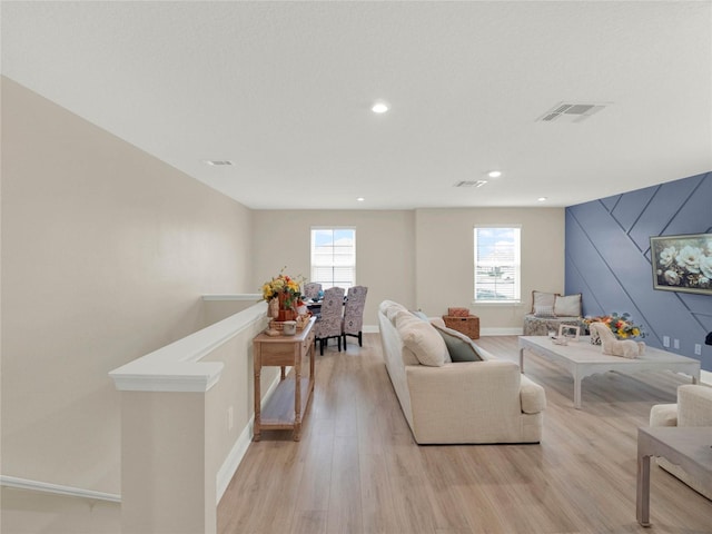 living room with light wood-type flooring, plenty of natural light, visible vents, and baseboards