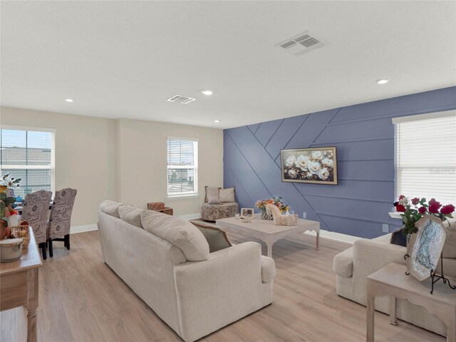 living room featuring an accent wall, light wood finished floors, visible vents, and baseboards