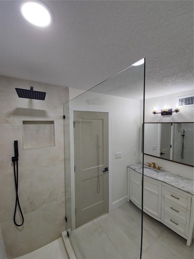 bathroom with baseboards, visible vents, walk in shower, a textured ceiling, and vanity