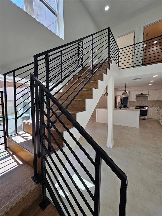 stairs featuring recessed lighting, a high ceiling, and wood finished floors