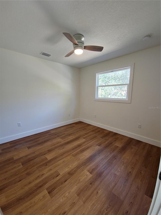 empty room featuring dark wood-style floors, visible vents, and baseboards