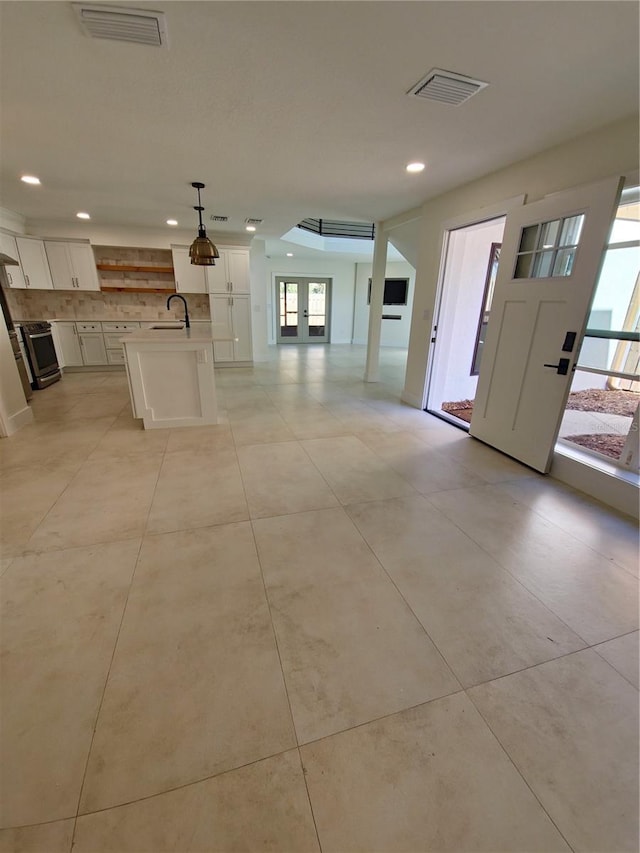 kitchen with light countertops, hanging light fixtures, visible vents, open floor plan, and an island with sink