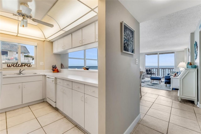 kitchen with light tile patterned floors, light countertops, a water view, white cabinets, and dishwasher