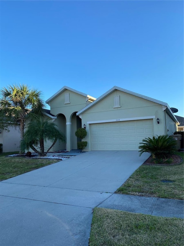 ranch-style home featuring concrete driveway, stucco siding, an attached garage, and a front yard