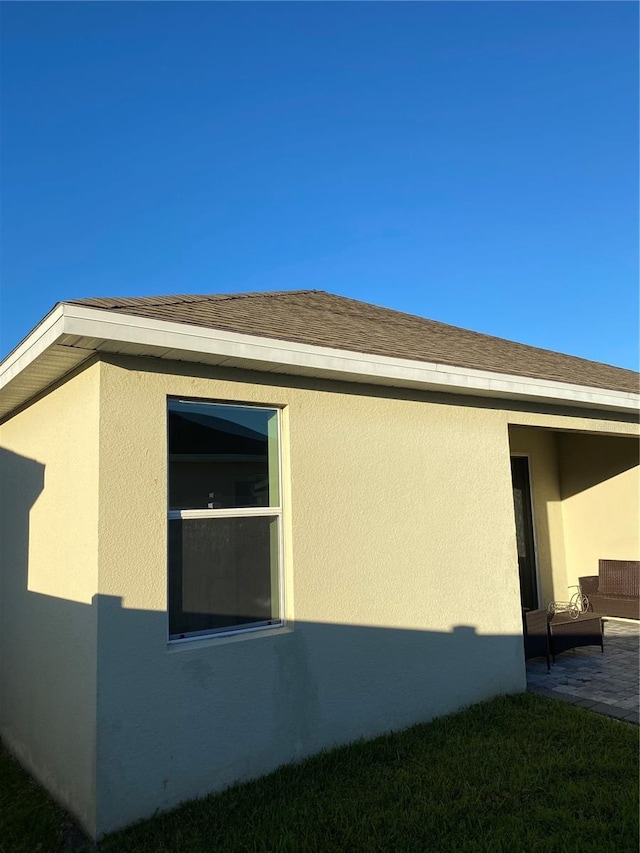 view of side of home with stucco siding and a shingled roof