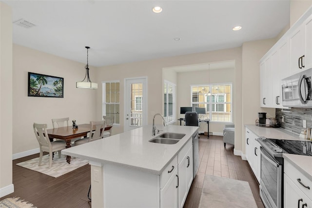 kitchen with a kitchen island with sink, a sink, light countertops, appliances with stainless steel finishes, and decorative light fixtures