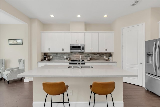 kitchen with appliances with stainless steel finishes, white cabinetry, a sink, and an island with sink