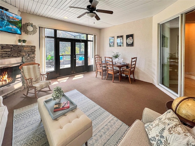 sunroom / solarium with ceiling fan, a stone fireplace, wood ceiling, and french doors