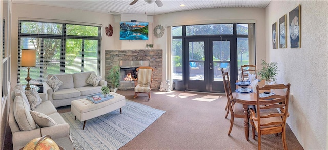 carpeted living room featuring ceiling fan, a stone fireplace, and french doors