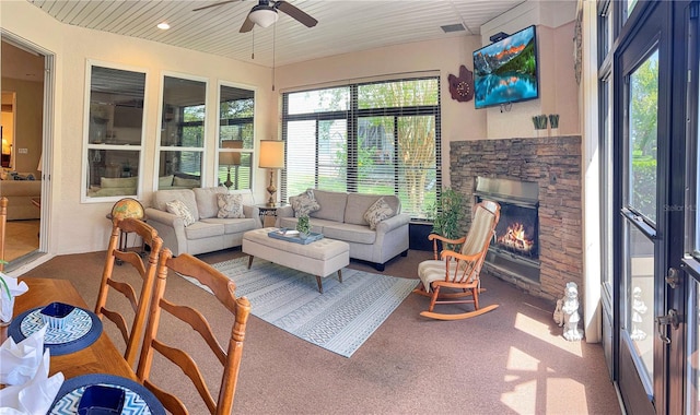 sunroom with ceiling fan and a stone fireplace