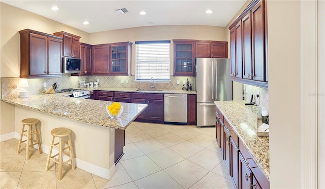 kitchen with a breakfast bar, light stone countertops, sink, backsplash, and appliances with stainless steel finishes