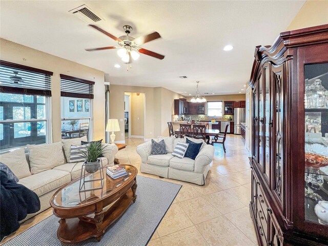 tiled living room with ceiling fan with notable chandelier