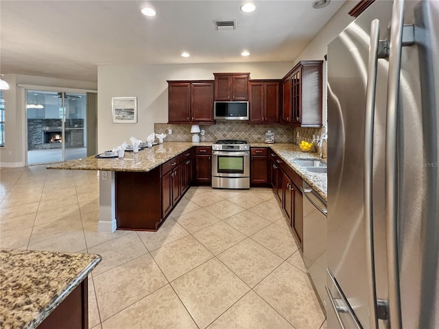 172 Balmy Coast Rd, Groveland, FL 34736 - kitchen featuring appliances with stainless steel finishes, a peninsula, light tile patterned floors, tasteful backsplash, and light stone countertops