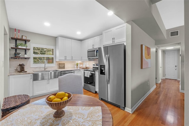 kitchen with white cabinets, light wood-type flooring, stainless steel appliances, and sink