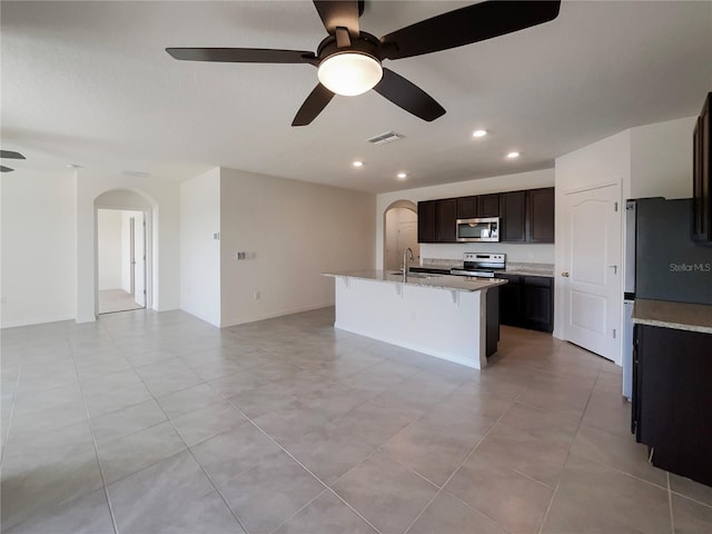 kitchen featuring stainless steel appliances, arched walkways, visible vents, and an island with sink