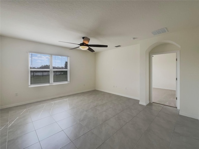 empty room with light tile patterned floors, a ceiling fan, visible vents, and a textured ceiling