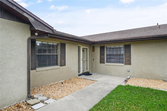 property entrance with roof with shingles and stucco siding