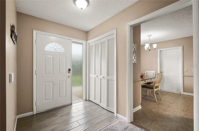 entryway featuring a textured ceiling, baseboards, a notable chandelier, and wood finished floors