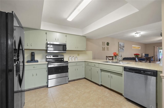 kitchen featuring green cabinetry, a peninsula, stainless steel appliances, light countertops, and a sink