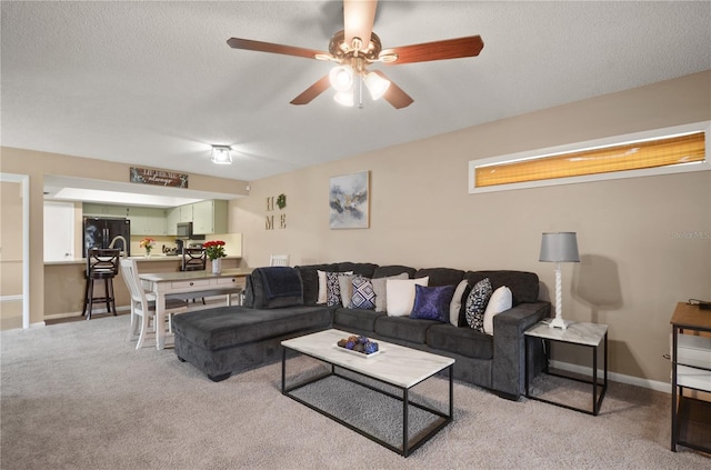 living room featuring light carpet, ceiling fan, baseboards, and a textured ceiling