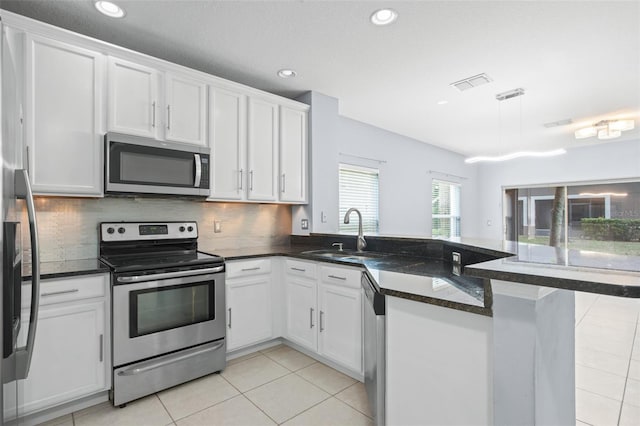 kitchen with light tile patterned floors, stainless steel appliances, a peninsula, a sink, and white cabinetry