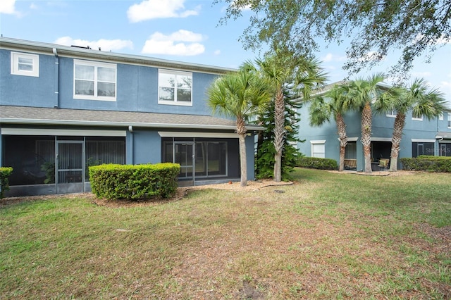 rear view of property featuring a sunroom, a lawn, and stucco siding