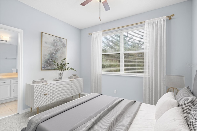 bedroom with a ceiling fan, light colored carpet, and ensuite bath