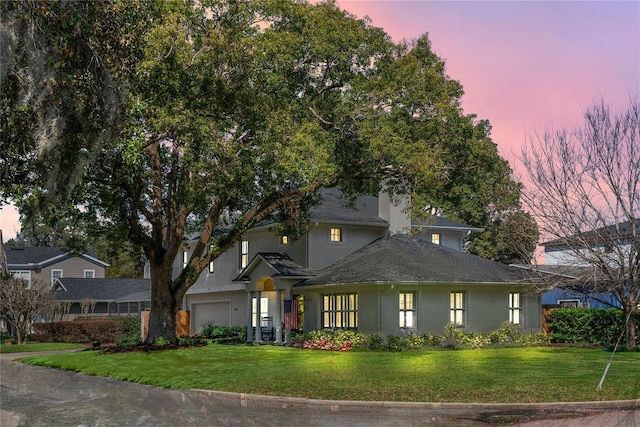 traditional-style home featuring a yard, a chimney, an attached garage, and stucco siding