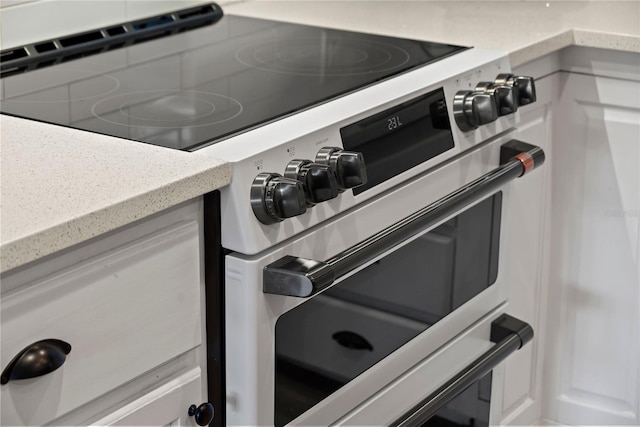 room details with white cabinets, double oven range, and light stone countertops