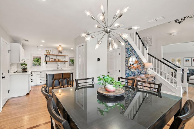 dining room featuring visible vents, stairs, light wood-type flooring, plenty of natural light, and an inviting chandelier